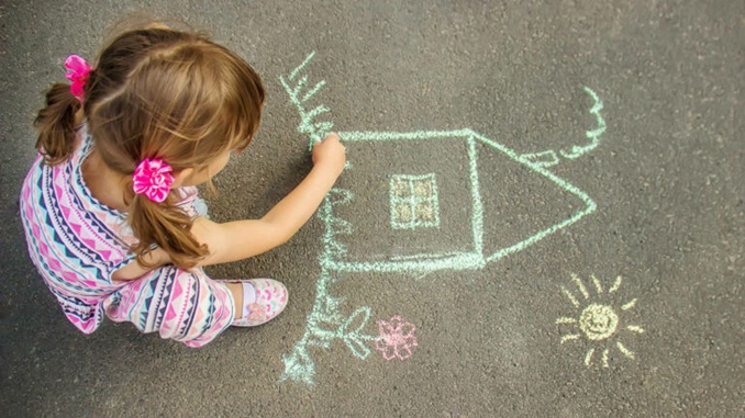 The child draws the house with chalk on the asphalt. Selective focus.